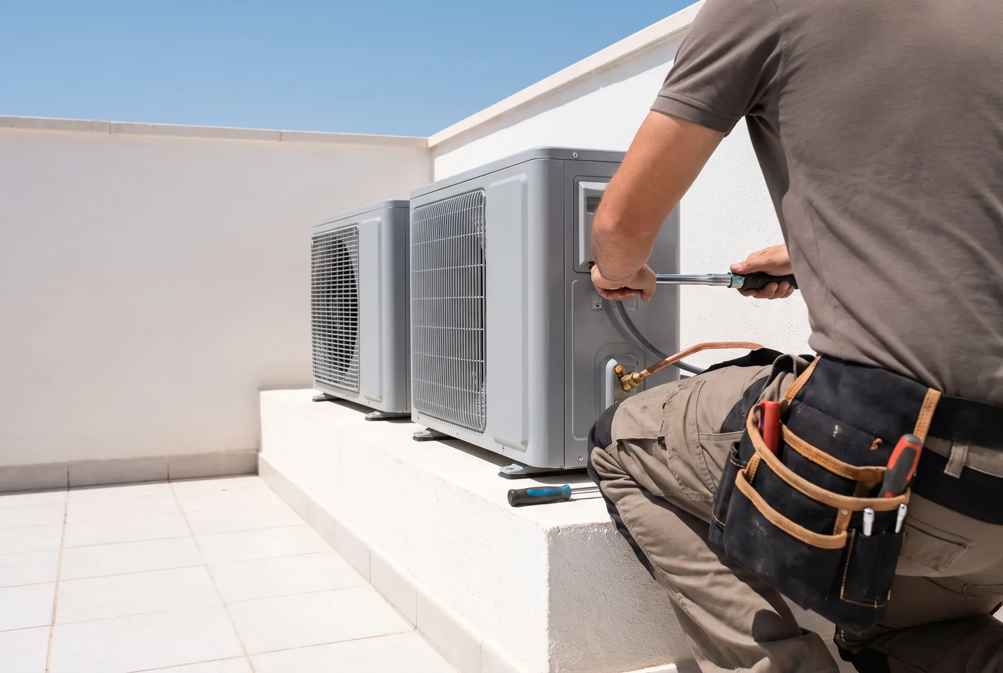 Technician tightening a refrigerant line on condenser units aligned on a villa terrace